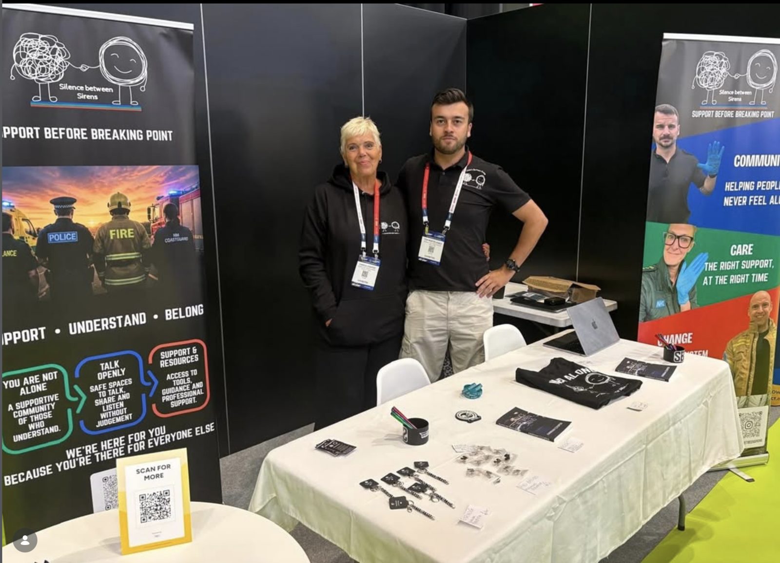 Two members of the Silence Between Sirens team at our stand at The Emergency Services Show, with banners, books and merchandise